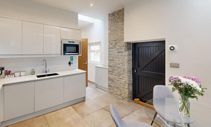 A bright and spacious kitchen with a glass dining table, exposed stonework, and a black stable door.
